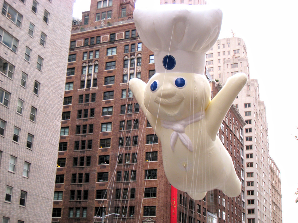 Macy's Thanksgiving Day parade on Nov 24, 2016, looking up at the Pillsbury Dough Boy float and ropes visible against the skyscrapers in NYC